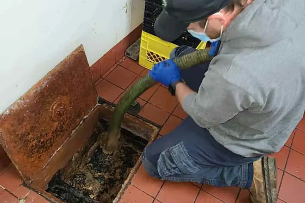 Plumber cleaning a kitchen drain with a vacuum hose for grease trap service in Tampa