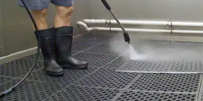 Person pressure washing textured kitchen floor with high-pressure water.
